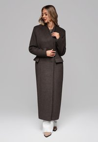 Brun uldblandingsfrakke med et skræddersyet design, der har en omslaglukning, sidelommer og minimalistiske detaljer. Lang, lige silhuet.