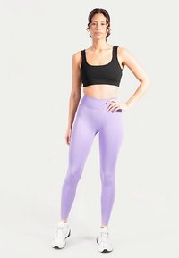 Schwarzer Sport-BH und lavendelfarbene Leggings aus Stretchgewebe mit hohem Bund und glatter Textur, kombiniert mit weißen Sportschuhen.