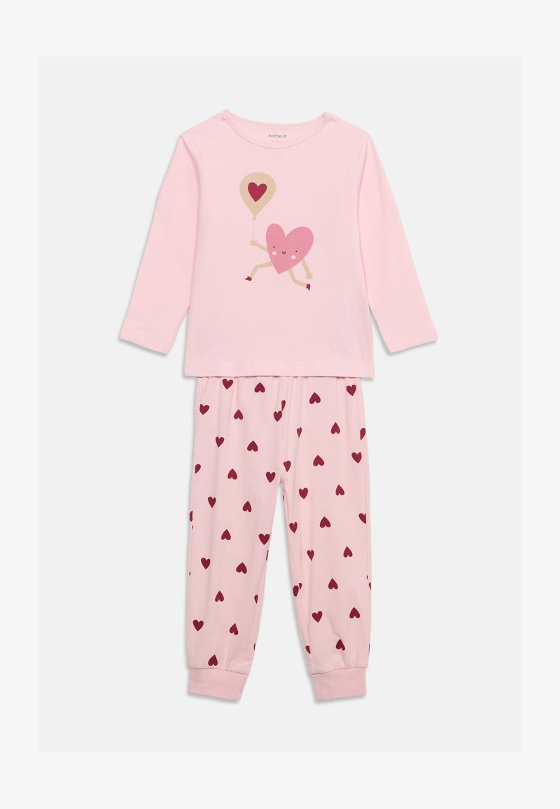 Haut rose à manches longues avec un cœur de dessin animé tenant un ballon et pantalon assorti avec des petits cœurs rouges en motif.