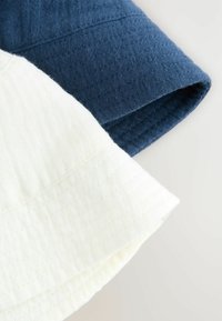 Zwei Stoffmuster: eines in Dunkelblau mit strukturierter Webart und das andere in Creme mit glatter Oberfläche, beide mit Kantenstich.