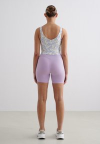 Floral-patterned tank top with a low back, paired with lavender bike shorts. Lightweight, fitted design. White athletic shoes and smooth texture.