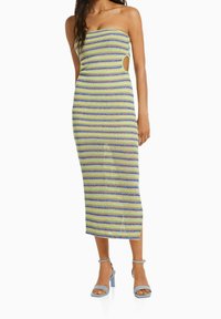 Robe midi sans bretelles présentant des rayures horizontales bleues et vertes, un design ajusté et des découpes latérales. Associée à des sandales à talons carrés bleu clair.