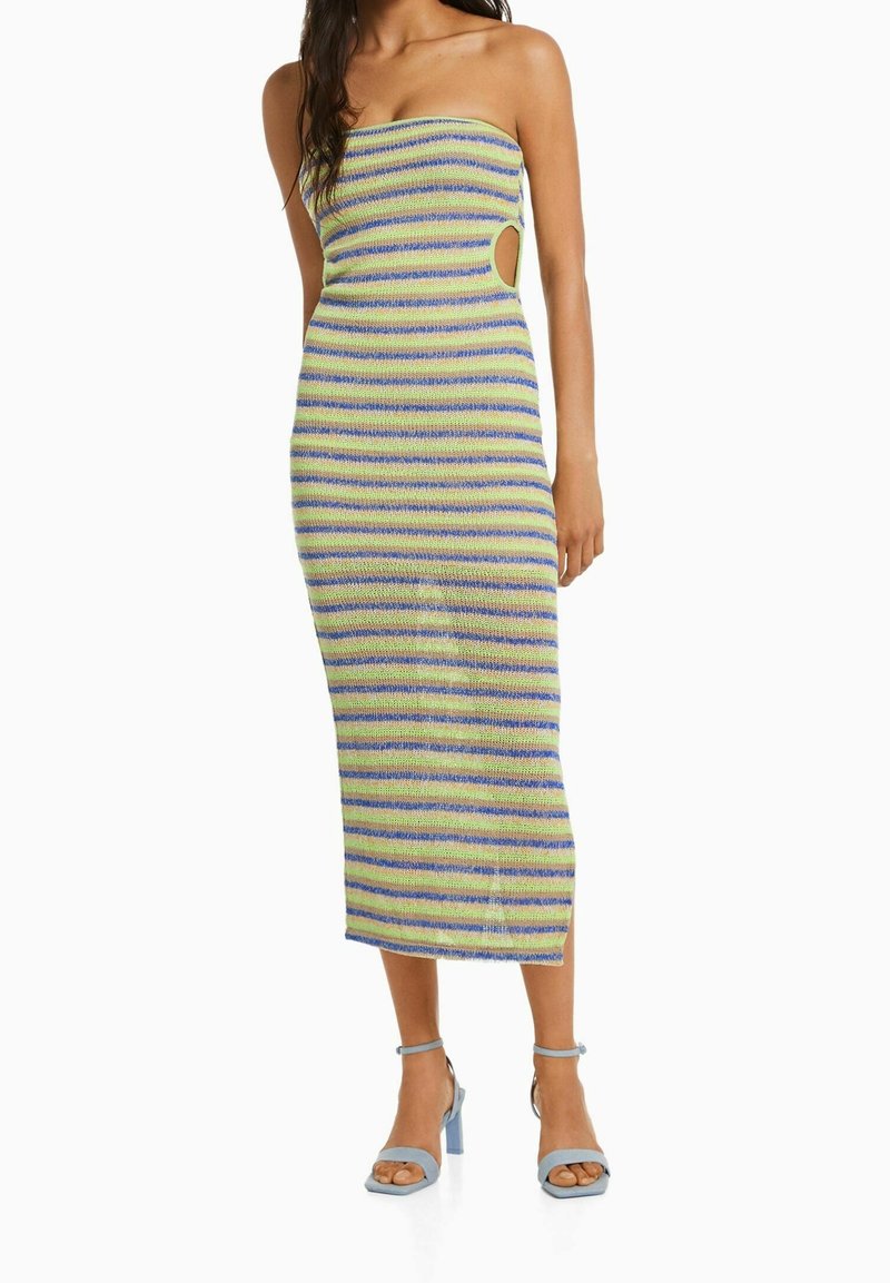 Robe midi sans bretelles présentant des rayures horizontales bleues et vertes, un design ajusté et des découpes latérales. Associée à des sandales à talons carrés bleu clair.