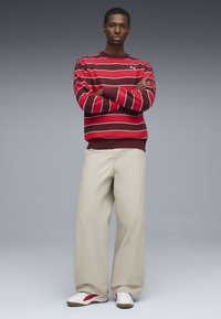 Felpa a righe rosse e bianche con colletto a girocollo, abbinata a pantaloni beige larghi. Footwear presenta un'accenno rosso su sneakers bianche.