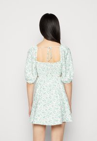 Vestido floral com mangas bufantes, padrão azul claro e branco, costas abertas seguras com laços, saia fluida, tecido macio, comprimento acima do joelho.