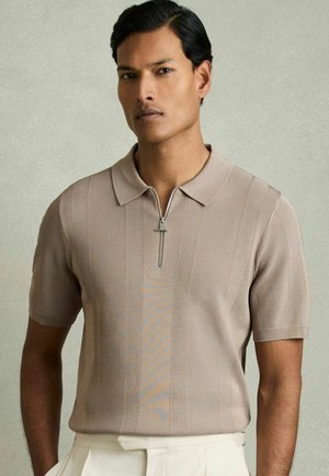 Polo majica kratkih rukava, bež boje s zatvaranjem na zip i suptilnom vertikalnom rebrastom teksturom. Ima kontrastne narančaste šavove.