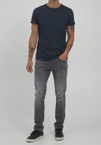 Camiseta azul marino de cuello redondo con bolsillo, combinada con jeans gris claro con detalles sutilmente desgastados. Zapatillas negras completan el look.