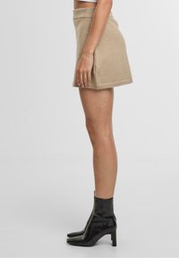 Beige stickad minikjol med hög midja och sidorslitsar, kombinerad med svarta ankelboots. Tyget verkar mjukt och strukturerat.