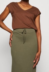 Top marrón de manga corta y escote en V combinado con una falda larga ajustada de color verde oliva que cuenta con una cintura ajustable. Tela suave y elástica.