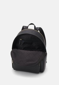 Sac à dos en cuir noir de forme arrondie, avec des garnitures dorées et un intérieur en tissu noir matelassé. Il dispose d'une poche zippée à l'intérieur.