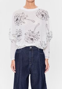 Lätt, vit långärmad topp med svart blommönster. Mjuk textur, lös passform, kombinerad med mörka denim, högmidjade byxor.