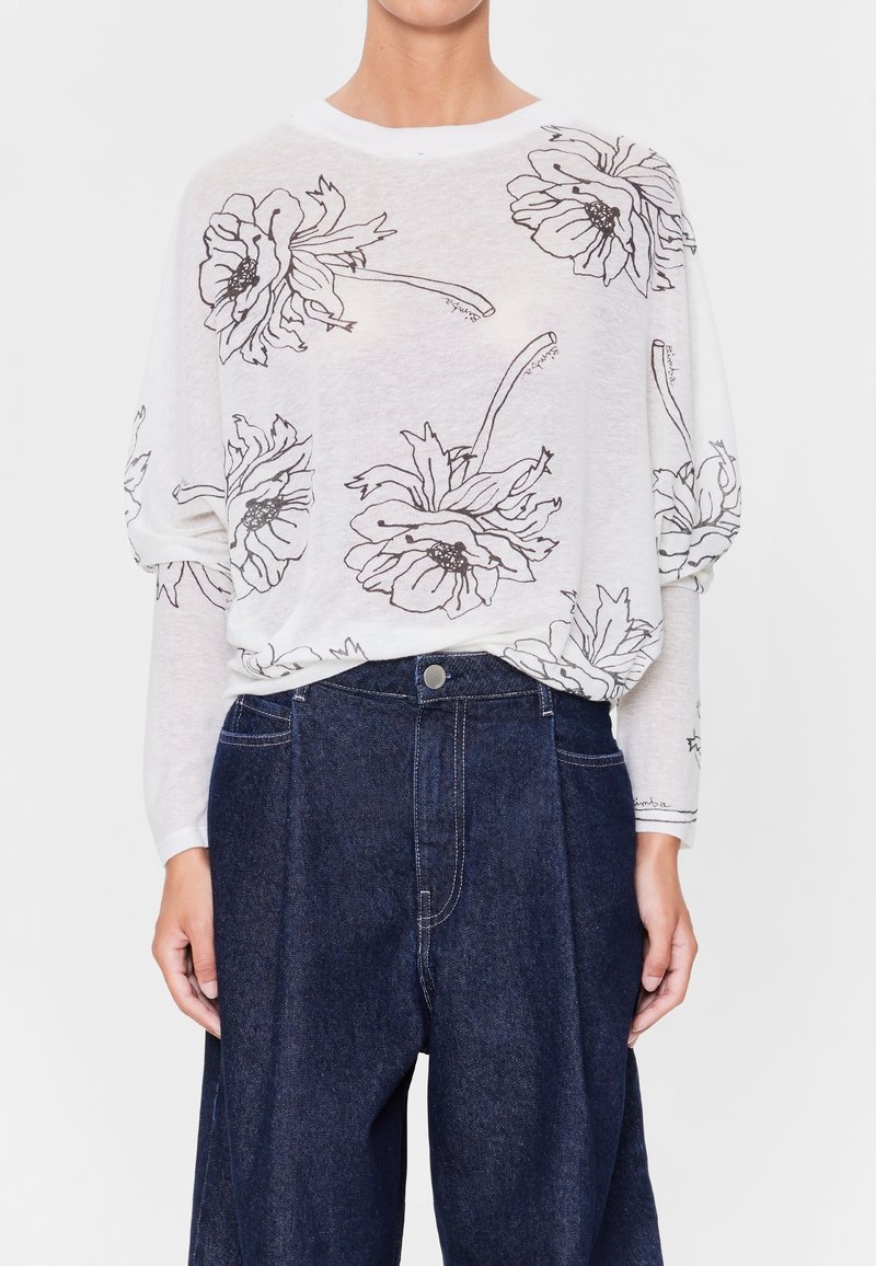 Lätt, vit långärmad topp med svart blommönster. Mjuk textur, lös passform, kombinerad med mörka denim, högmidjade byxor.