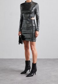 Czarna sukienka cekinowa z długimi rękawami, z bocznym wycięciem; zestawiona z czarnymi botkami do kostki z ostro zakończonym noskiem i detalem na suwak.