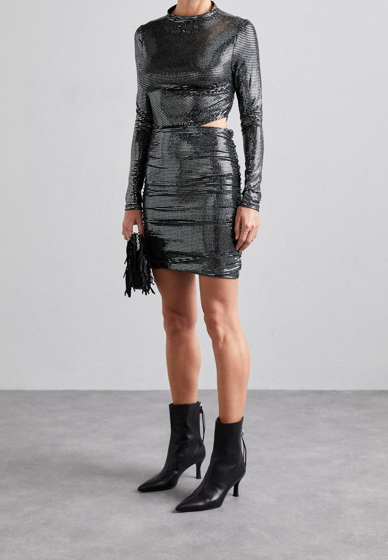 Czarna sukienka cekinowa z długimi rękawami, z bocznym wycięciem; zestawiona z czarnymi botkami do kostki z ostro zakończonym noskiem i detalem na suwak.