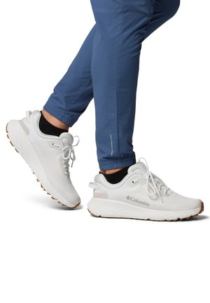 Beine in blauen Jogginghosen und schwarzen Knöchelsocken, getragen mit weißen Columbia-Sportschuhen mit Schnürsenkeln und Sohlen aus Gummimischung.