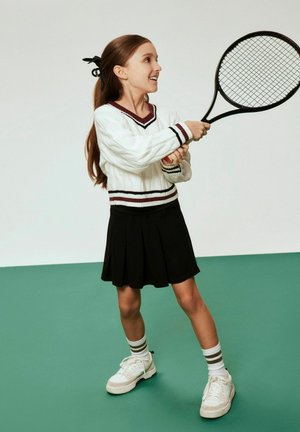 White cable-knit sweater with burgundy accents, black pleated skirt, and white sneaker with grey stripes on socks, holding a tennis racket.