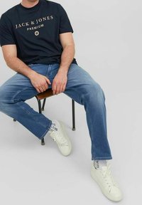 Camiseta de manga corta azul marino oscuro con texto dorado "JACK & JONES PREMIUM", combinada con vaqueros de mezclilla azul claro y zapatillas blancas con calcetines estampados.