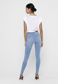 Jeans skinny de color azul claro hechos de denim, con una cintura alta, bolsillos traseros y una textura suave. Combinados con una blusa blanca de manga corta.