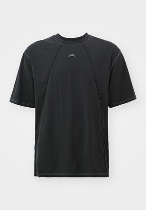 Camiseta negra de manga corta con cuello redondo, que presenta costuras en contraste y un pequeño logo en el pecho. Fabricada en suave material de algodón.