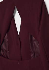 Blazer cintré bordeaux foncé avec ouverture avant, dévoilant une doublure satinée lisse à l'intérieur des panneaux et un détail de taille ajustée.