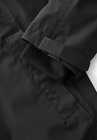 Tissu de veste imperméable noire avec une texture lisse, doté d'un revers roulé et d'une poche appliquée, complété par une doublure intérieure douce.