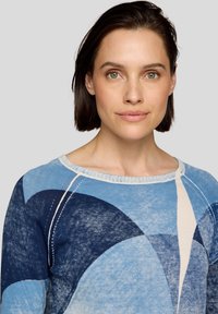 Strickpullover mit Rundhalsausschnitt und geometrischen Mustern in verschiedenen Blautönen, mit weißen Akzenten und einer strukturierten Oberfläche.