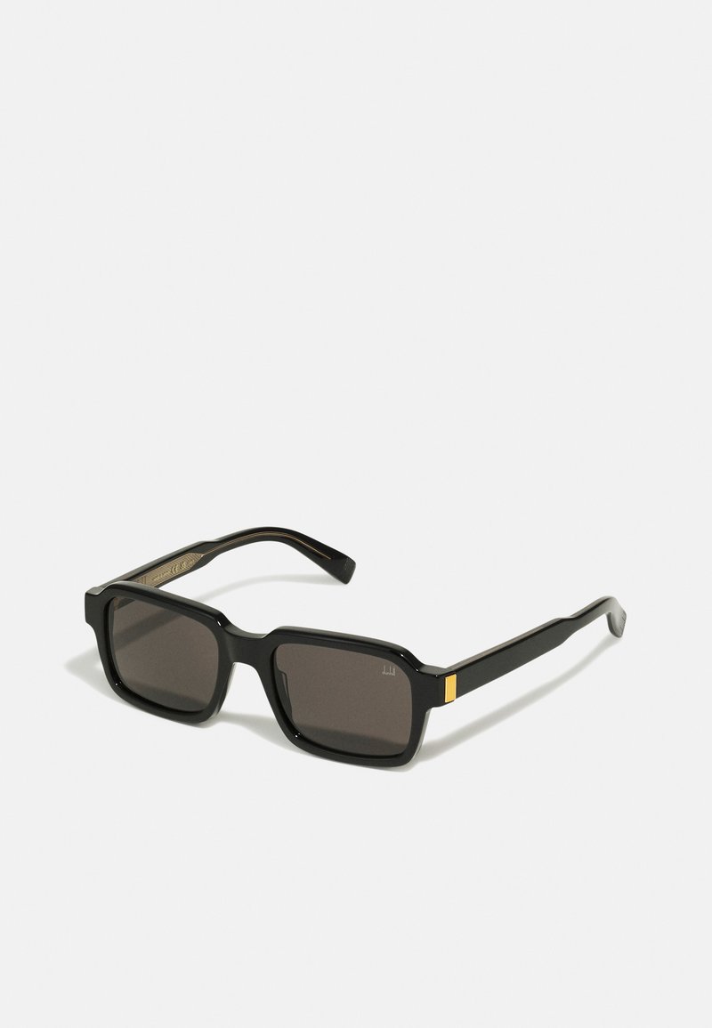 Occhiali da sole neri rettangolari con lenti scure, caratterizzati da un design elegante e un accentuazione dorata sulla tempia. Realizzati in plastica resistente.
