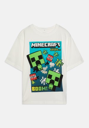 Bela bomba majica iz bombaža, ki prikazuje grafiko iz Minecrafta. Oblikovanje vključuje zelene like, besedilo "BOOM!" in TNT elemente v živahnih barvah.