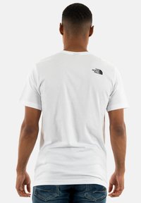 Camiseta blanca de manga corta hecha de algodón, con un logo negro minimalista en la parte superior de la espalda. Textura suave y corte clásico.