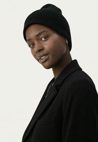 Svart ribbad mössa av stickat material, med en tät passform och en avsmalnad topp, bärs tillsammans med en svart blazer.