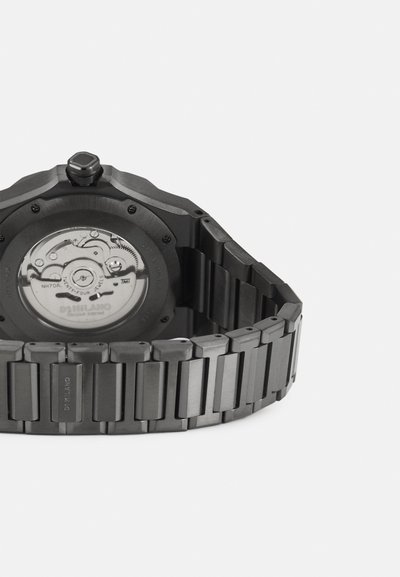 Schwarze Edelstahl-Uhr mit einem achteckigen Gehäuse, einem strukturierten Armband und einem transparenten Gehäuseboden, der das mechanische Uhrwerk zeigt.