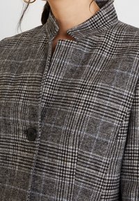 Uldblandet ternet blazer i grå og sort, med en mandarin-krave, knaplukning og subtile blå accenter i stofmønstret.