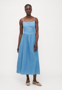 Vestido de mezclilla sin mangas de un azul claro, con una cintura definida y una falda fluida que llega hasta la mitad de la pantorrilla. Tirantes delgados ajustables y textura sutil.