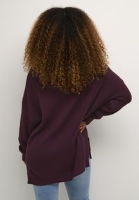 Overdimensioneret, ribbet lilla sweater med løs pasform, sideslidser og lange ærmer, parret med lyseblå jeans.