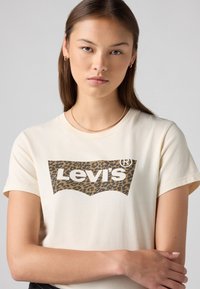 Kreminės spalvos trumpų Rankovių T-shirt, kuriame yra leopardų rašto Levi's logotipo grafika. Minkšta medžiaga, apvalus iškirpimas ir laisvas siluetas.