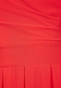 Czerwona pleciona sukienka z tkaniny o gładkiej fakturze, z ukośnymi detalami drapowania, tworzącymi strukturalny krój w intensywnym, jednolitym kolorze.