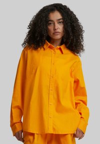 Oversized orange shirt made of lightweight fabric, featuring a button-down front, collar, and long sleeves with cuffs.