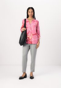 Rosa Hemd mit floralem Muster, graue Hose und schwarze Handtasche. Die Schuhe sind schwarze spitze Schuhe mit dekorativen Akzenten.