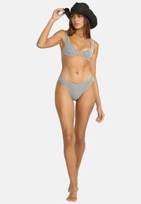 Bikiny s čierno-bielym kockovaným vzorom, s braletovým topom a vysoko vykrojenými spodkami. Modelka stojí na boso a má na sebe čierny slamenný klobúk.