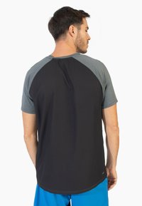 Camiseta deportiva masculina con un respaldo texturizado en negro y mangas raglán grises, que presenta una tela suave y un dobladillo redondeado.