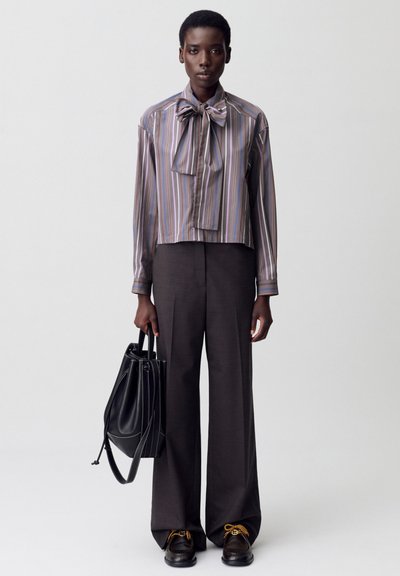 Blusa a righe corta in viola e beige con un grande fiocco, abbinata a pantaloni scuri a vita alta e gamba larga e scarpe nere con lacci gialli.