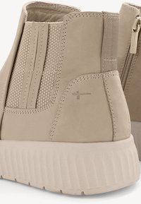 Bēša potīte ar teksturētu zamša augšdaļu, elastīgām sānu daļām un rievotu gumijas zoli. Iekļauta dekoratīva logo uz sāniem.