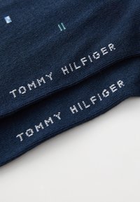 Marineblå sokker med lys blå og hvid tekst, der læser "TOMMY HILFIGER." Glat strikket tekstur, der har et enkelt design og brand. 