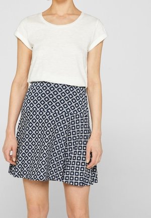 Weißes Kurzarmoberteil kombiniert mit einem marineblauen Rock mit Rautenmuster und ausgestelltem Saum aus leichtem Stoff.