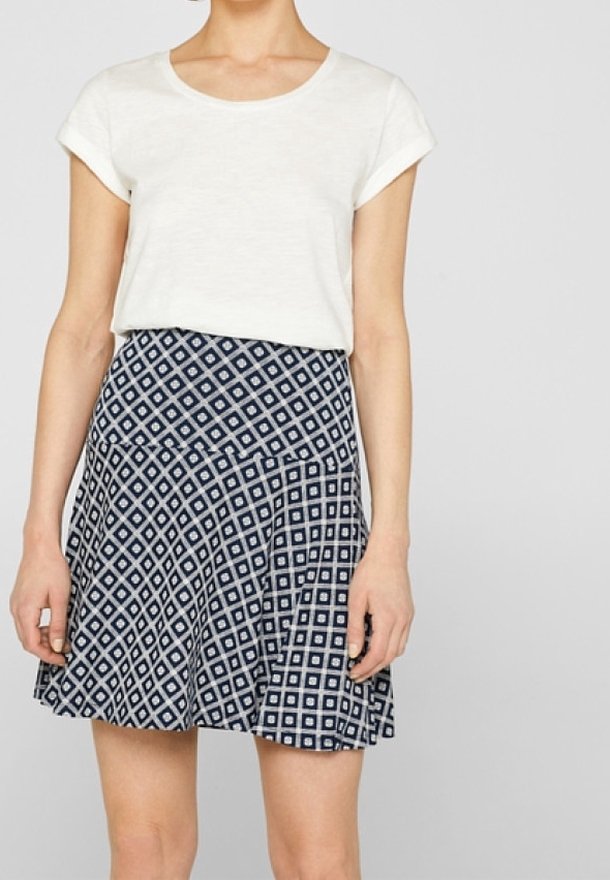 Haut blanc à manches courtes associé à une jupe bleu marine avec un motif en diamants et un ourlet évasé, fabriquée en tissu léger.