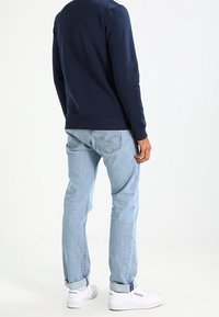 Námořnická mikina s dlouhými rukávy, světlé modré džíny a bílé tenisky. Džíny mají klasický design se pěti kapsami a viditelným šitím.