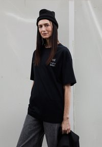 Melna, pārmēru liela t-krekls ar īsām piedurknēm un apaļu izgriezumu, priekšpusē ar nelielu izdruku — logotipu un tekstu. Kombinēts ar pelēkiem biksēm.