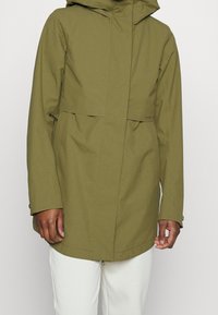 Oliwkowa wodoodporna kurtka z kapturem, kieszenią z przodu i zapięciem na zamek. Posiada luźny krój i regulowane mankiety.
