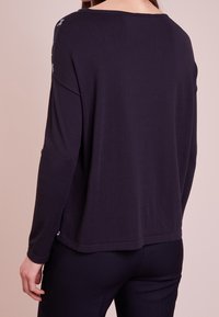 Maglione blu navy scuro realizzato in morbido tessuto, con una vestibilità comoda e maniche lunghe. Ricca ricamo floreale lungo le cuciture delle spalle.