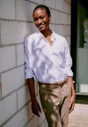 White button-up shirt with rolled sleeves; tan trousers with a brown belt. Smooth fabric, relaxed fit, and minimal embellishments.